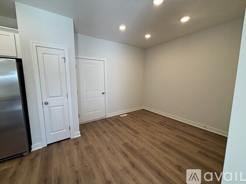A kitchen with a refrigerator, two doors, and wooden flooring.