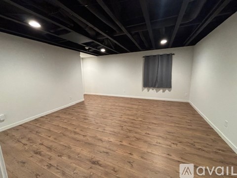 A room with wooden flooring and a window with a grey curtain.