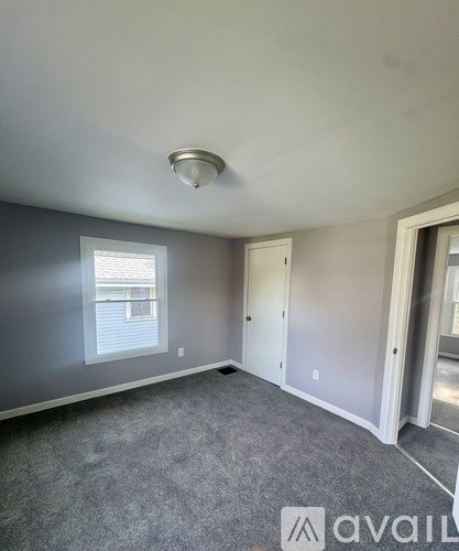 A room with grey carpet and a window with blinds.
