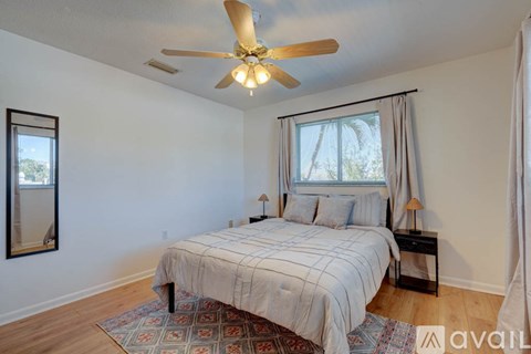 A bedroom with a bed, a ceiling fan, and a window with curtains.