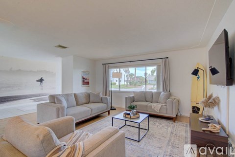 A living room with a large window, a sofa, a chair, a coffee table, and a flat-screen TV.