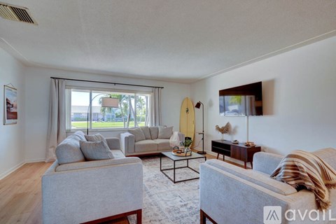 A living room with a grey couch, a coffee table, and a surfboard on the wall.