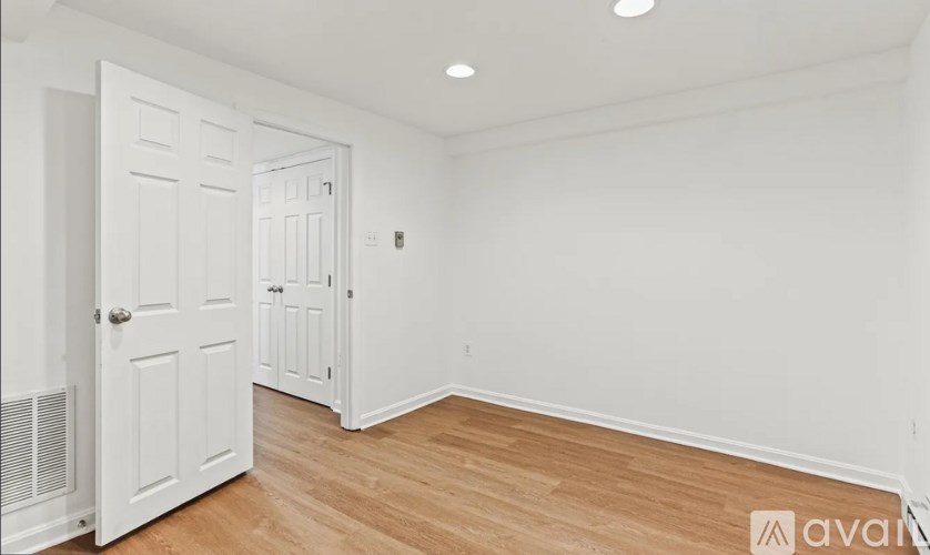A room with white walls and wooden flooring with a door on the left.