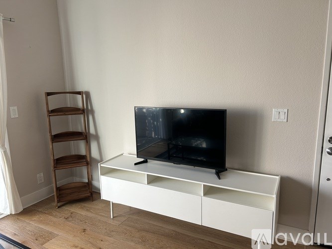 A black television sits on a white stand with a wooden shelf to its left.