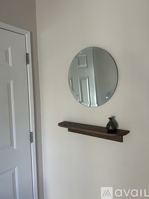 A white door is to the left of a round mirror and a shelf with a vase on it.