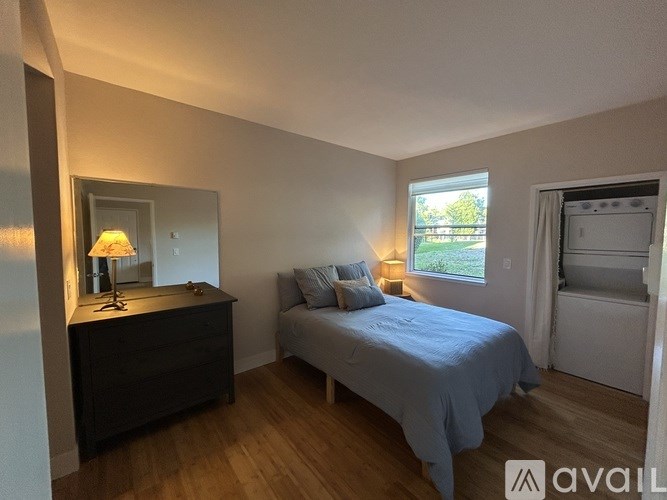 A bedroom with a bed, nightstand, and a window with a view of greenery outside.