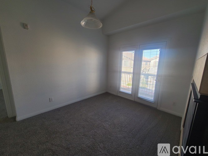 A room with a carpeted floor, a window with blinds, and a hanging light fixture.