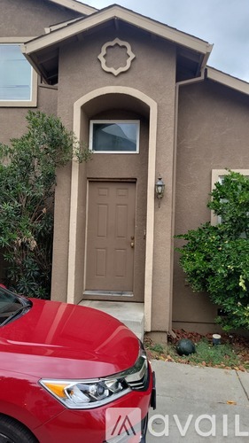 A red car is parked in front of a house with a brown door.