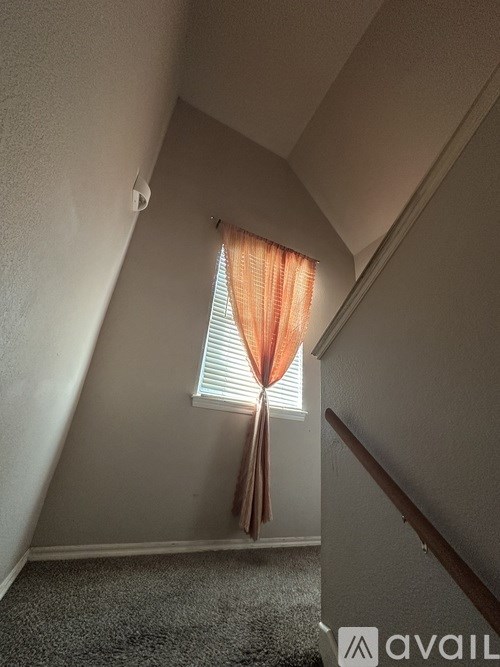 A hallway with a carpeted floor and a window with orange curtains.