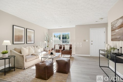 A living room with a white couch, a brown ottoman, and a glass coffee table.