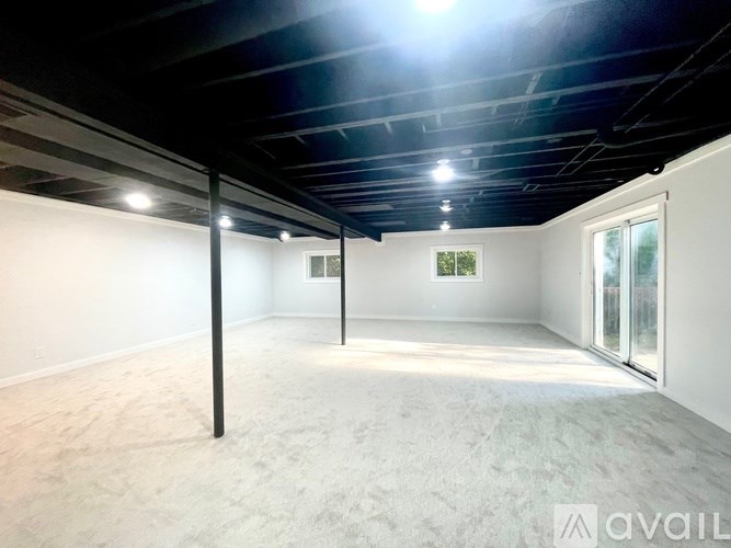 A spacious room with a carpeted floor and a window on the right side.