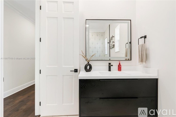 A bathroom with a white door, a mirror, and a black vanity.