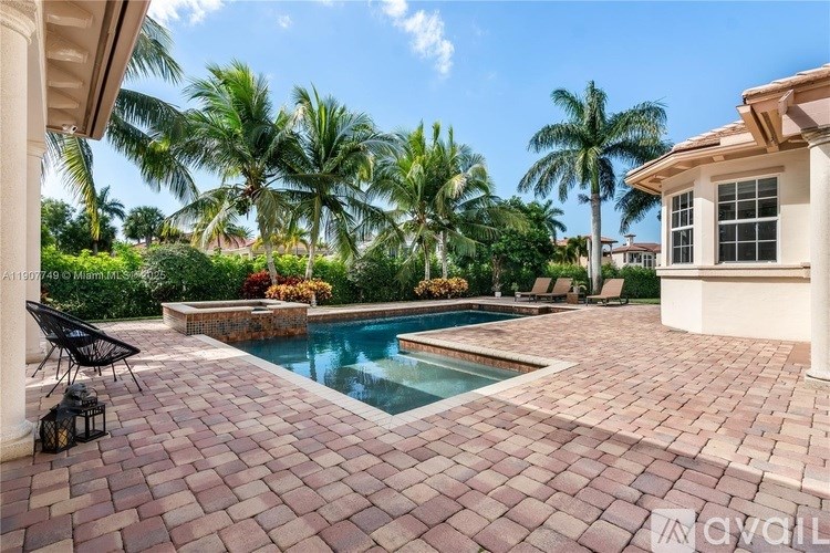 A pool surrounded by a brick patio and palm trees.