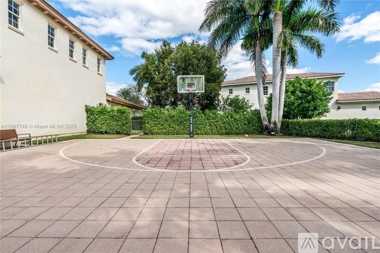 A basketball court is surrounded by a white wall and a palm tree.