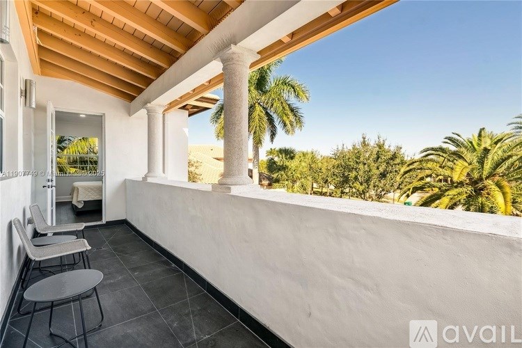 A balcony with a table and chairs overlooking a palm tree lined beach.