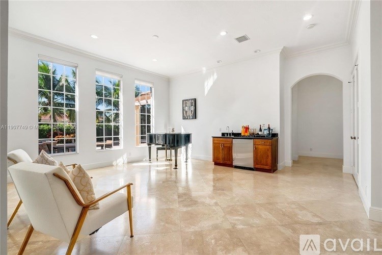 A spacious living room with a large window, a sofa, a chair, and a kitchen area in the background.