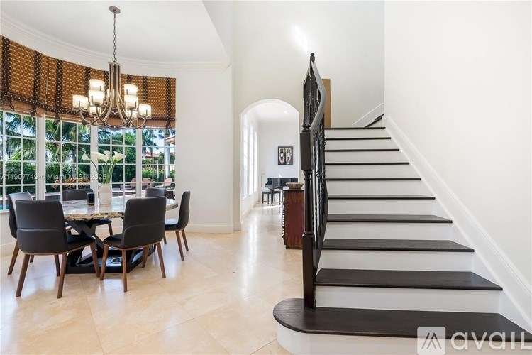 A modern dining room with a chandelier, a dining table with chairs, and a staircase.