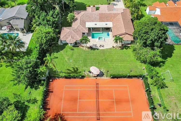 A tennis court is located in the middle of a lush green yard.