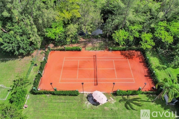An aerial view of a tennis court surrounded by greenery.