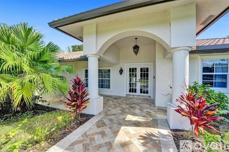 A white house with a porch and a palm tree.