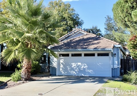 A house with a white garage door is surrounded by greenery.