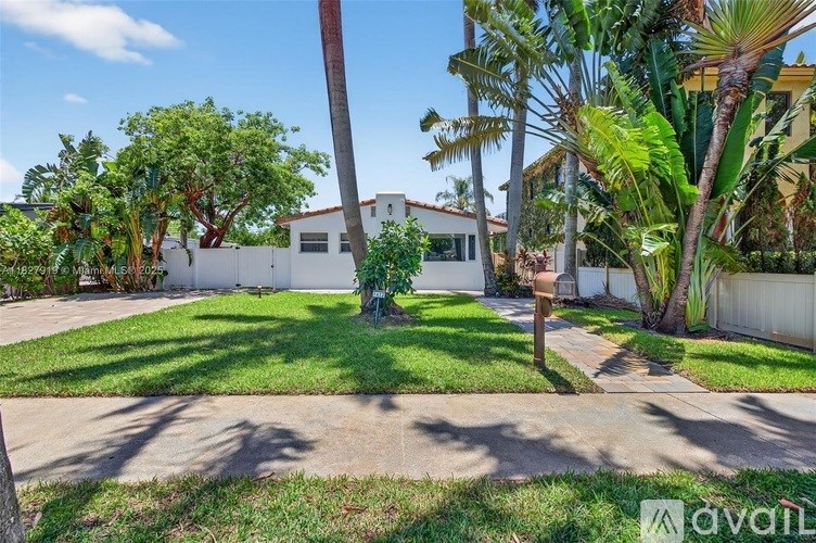 A white house with a green lawn and palm trees in front.