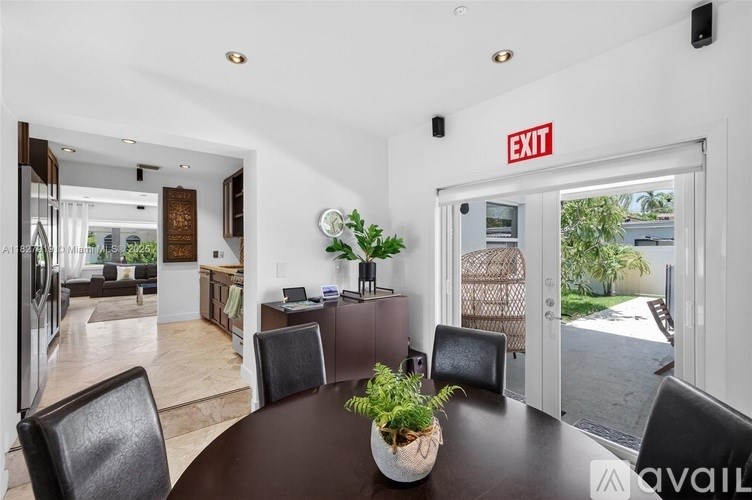 A modern dining room with a round table and chairs, a potted plant, and a view of the backyard through the sliding glass door.