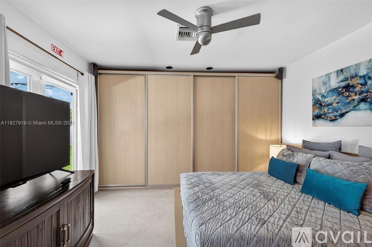 A bedroom with a bed, a ceiling fan, and a television.