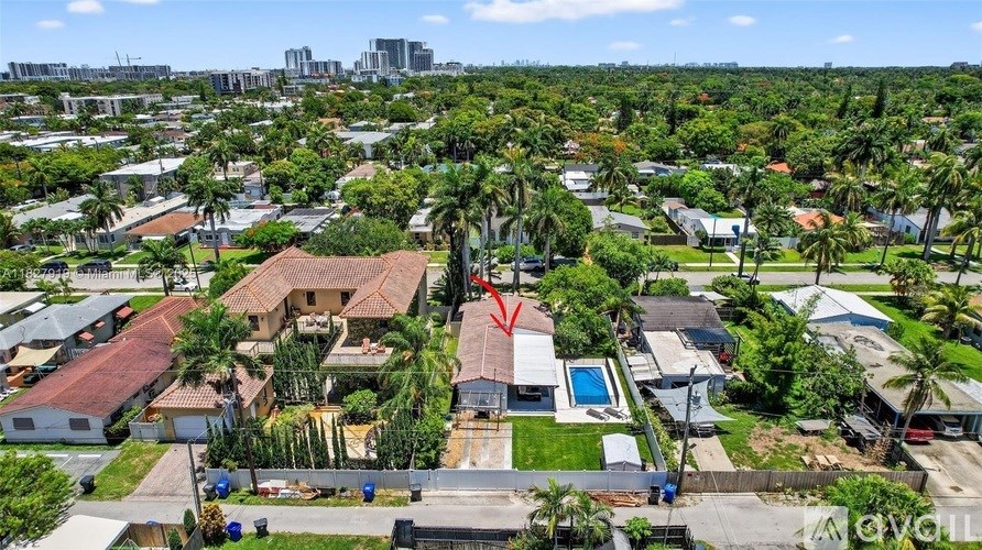 A bird's eye view of a residential area with a house in the foreground and a city skyline in the background.