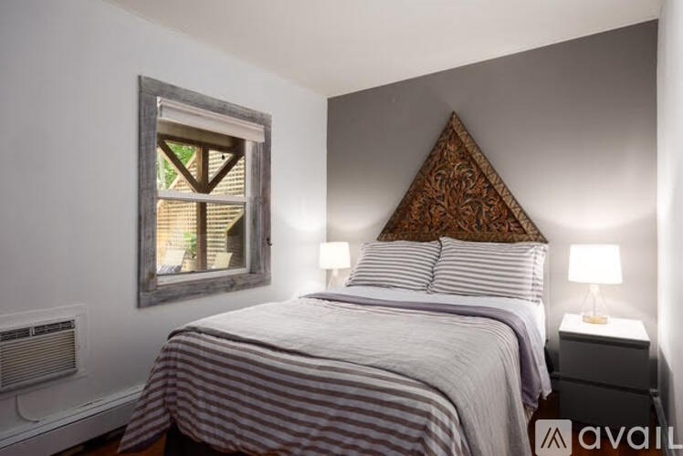 A bedroom with a bed, two lamps, and a window with a view of trees.
