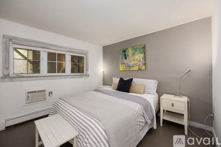 A bedroom with a bed, nightstand, and a window.