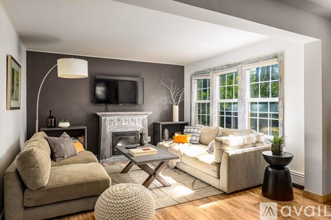 A living room with a grey couch, a white armchair, a coffee table, a fireplace, and a television on the wall.