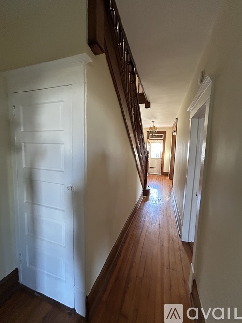 A hallway with a white door on the left and a wooden staircase on the right.