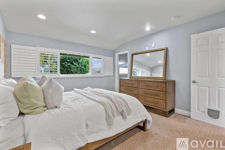 A bedroom with a bed, dresser, mirror, and window with blinds.