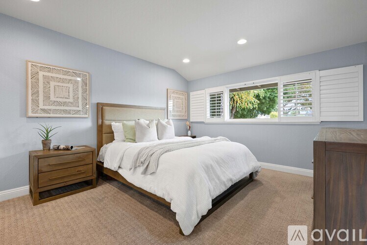 A bedroom with a large bed, a nightstand, and a window with blinds.