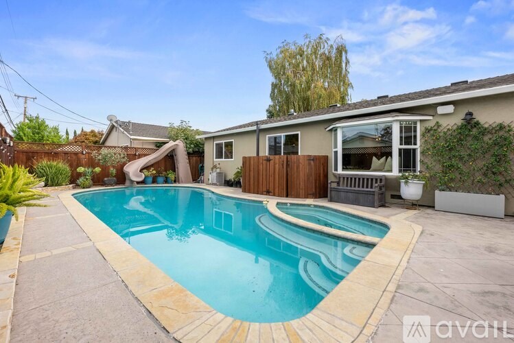A swimming pool in a backyard with a wooden fence and a house in the background.