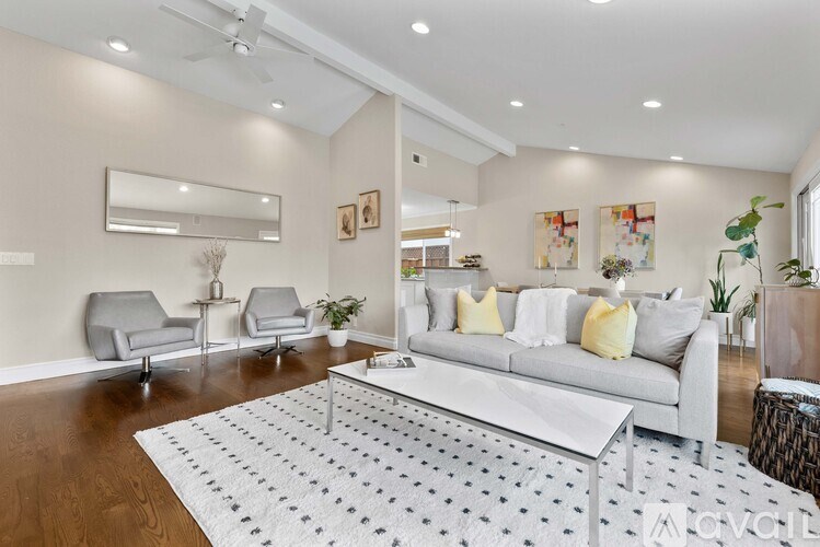 A living room with a white couch, grey chairs, and a patterned rug.