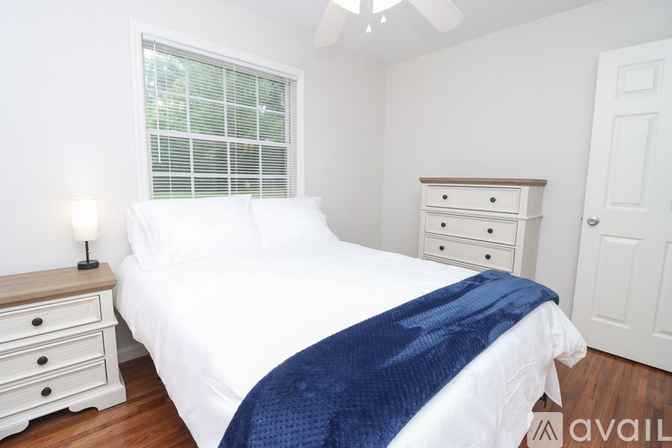 A bedroom with a white bed, blue blanket, and a white dresser.