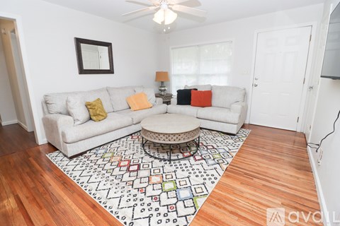 A living room with a white couch, a rug with a pattern, and a ceiling fan.