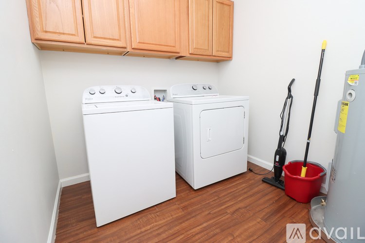 A room with a washer and dryer and a red bucket and a vacuum cleaner.
