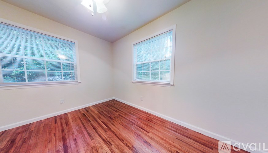 A room with wooden flooring and two windows.