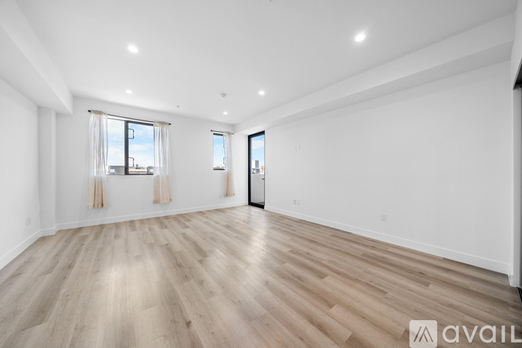 A spacious room with wooden flooring and two windows.
