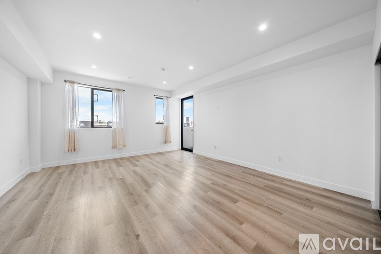 A spacious room with wooden flooring and two windows.