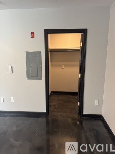 A black door with a glass window is open to a room with a white wall and a grey electrical box.