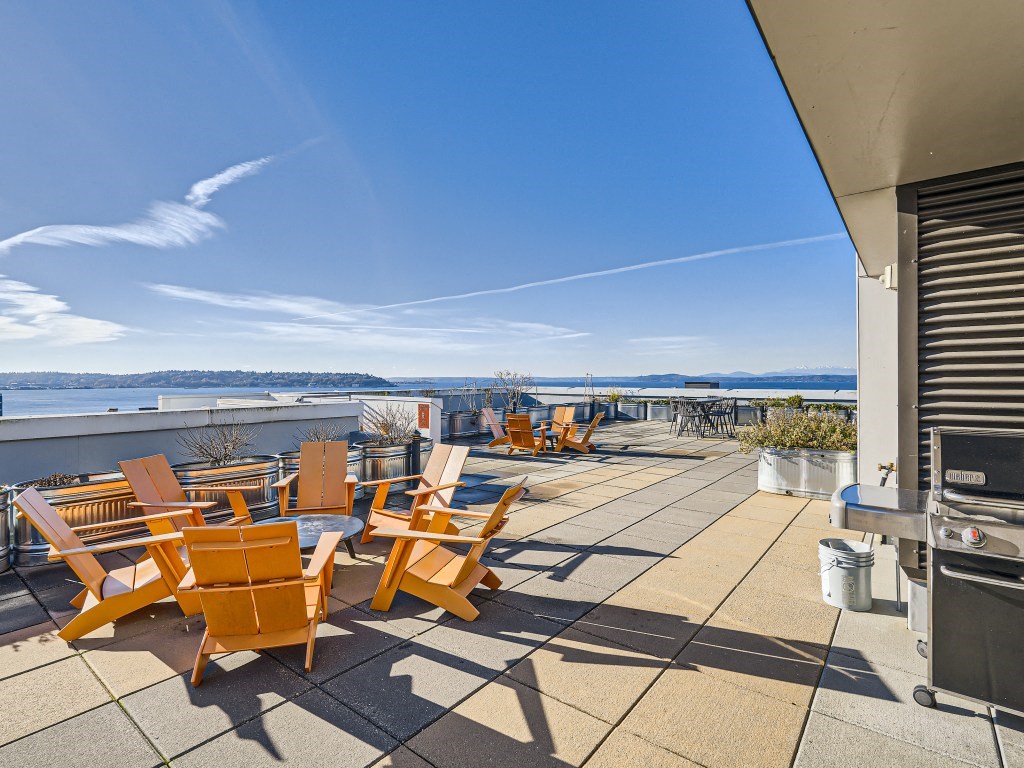 a patio with chairs and a grill and a view of the water