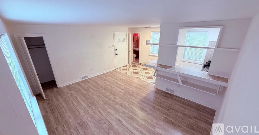 A room with wooden flooring and white walls, with a window on the right side.