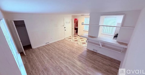 A room with wooden flooring and white walls, with a window on the right side.