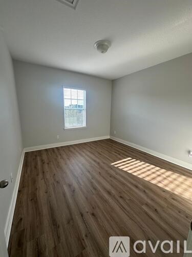 A room with wooden flooring and a window letting in sunlight.