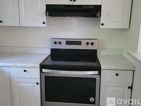 A black stove top oven with four burners and a digital display is installed in a kitchen with white cabinets.