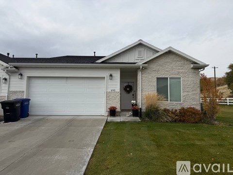 A house with a white garage door and a blue trash bin in front of it.